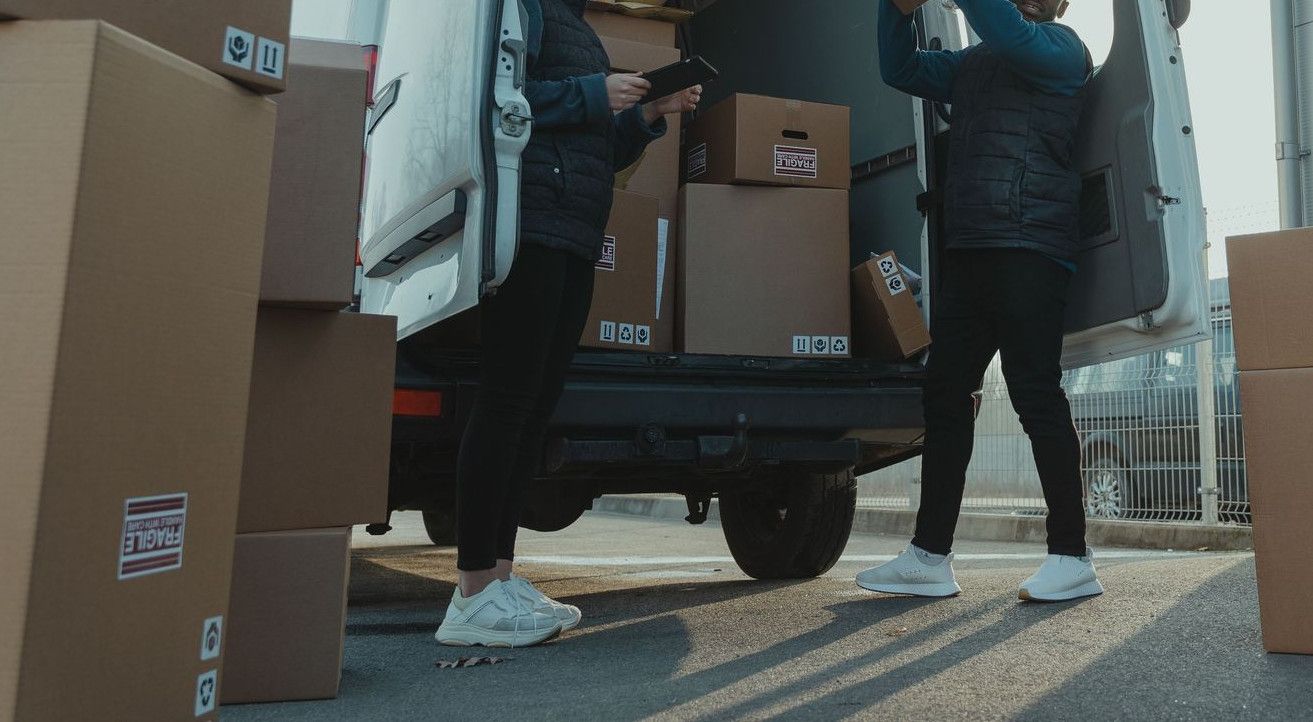 Workers loading boxes into a delivery van at a warehouse facility outdoors.