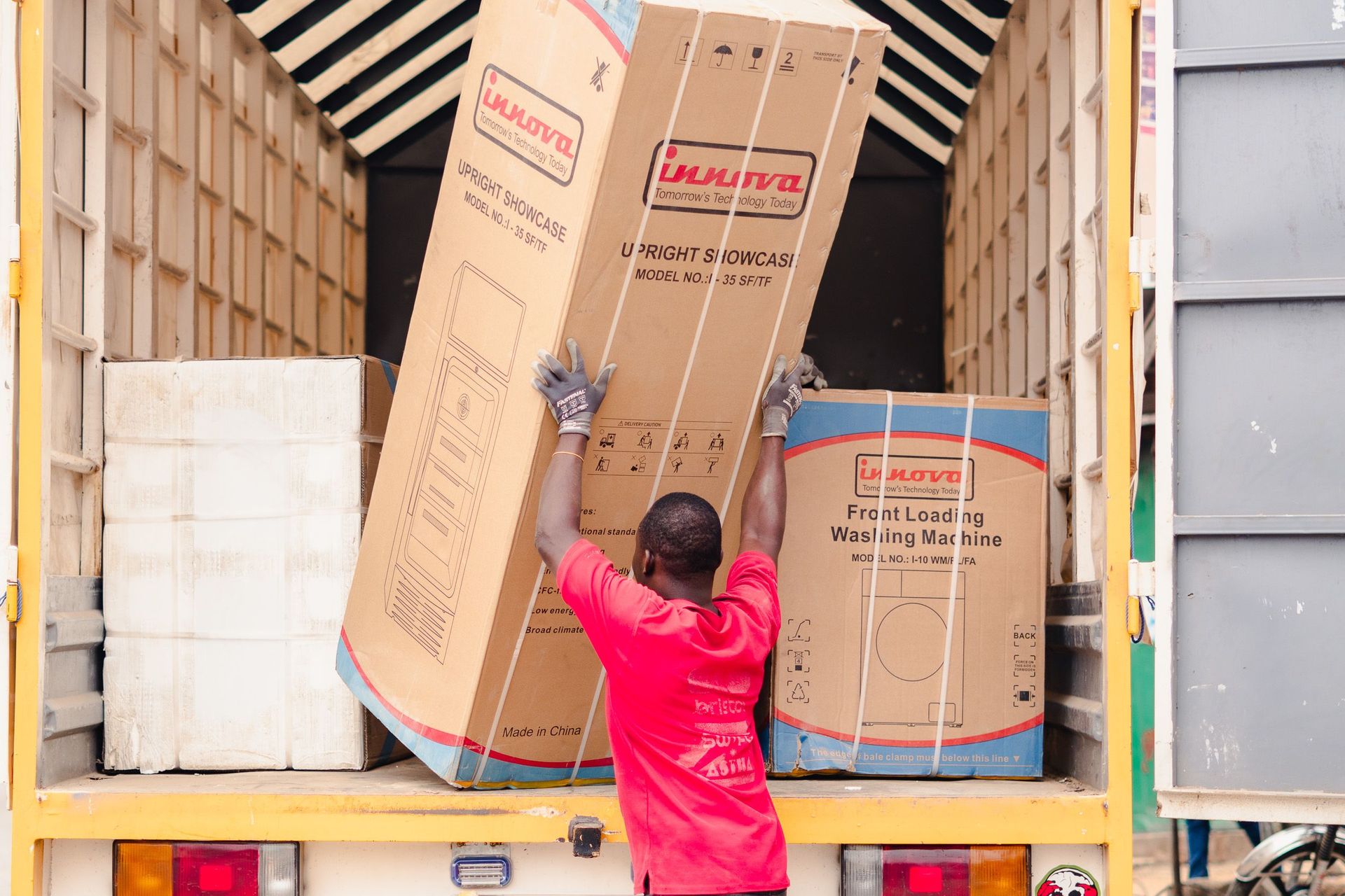 A worker in a red shirt loads boxed appliances onto a truck for delivery.