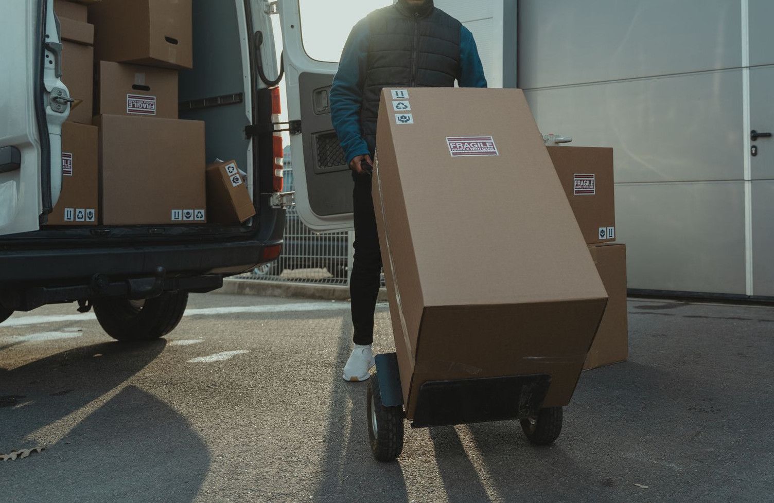 Delivery man with trolley unloading boxes from a van outside a warehouse.