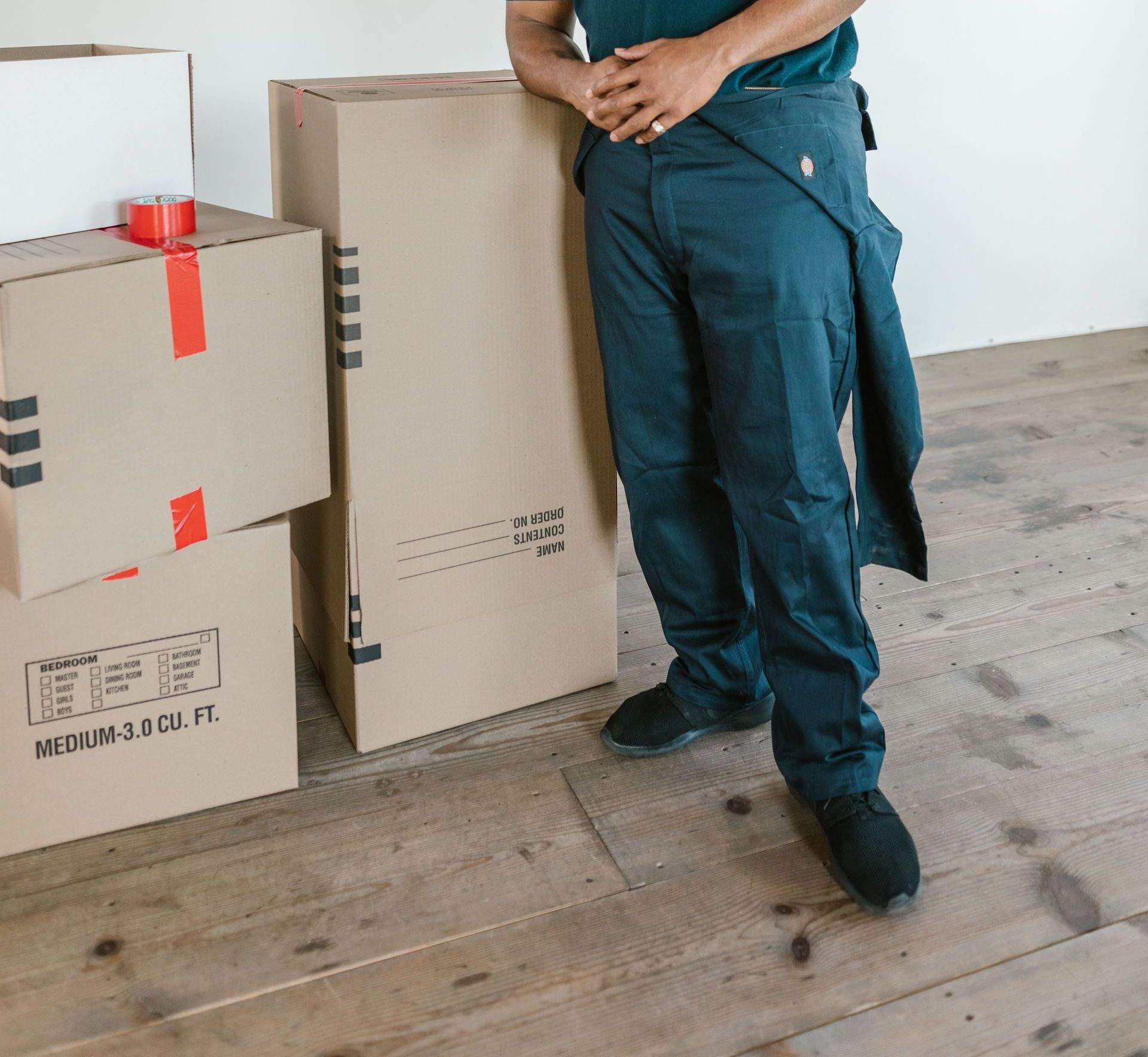 Smiling delivery worker in uniform standing with packaged boxes indoors.